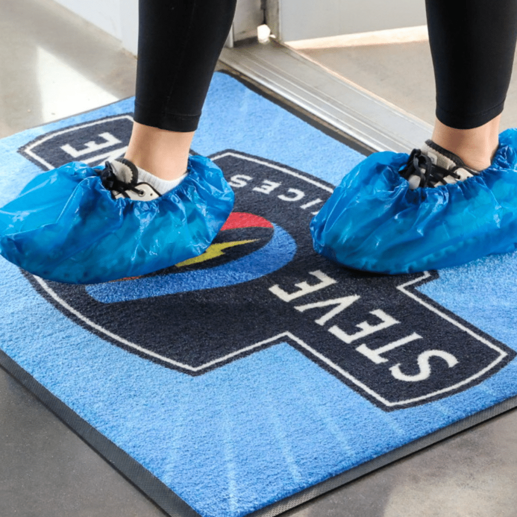 Technician wearing blue shoe covers standing on custom logo entry mat
