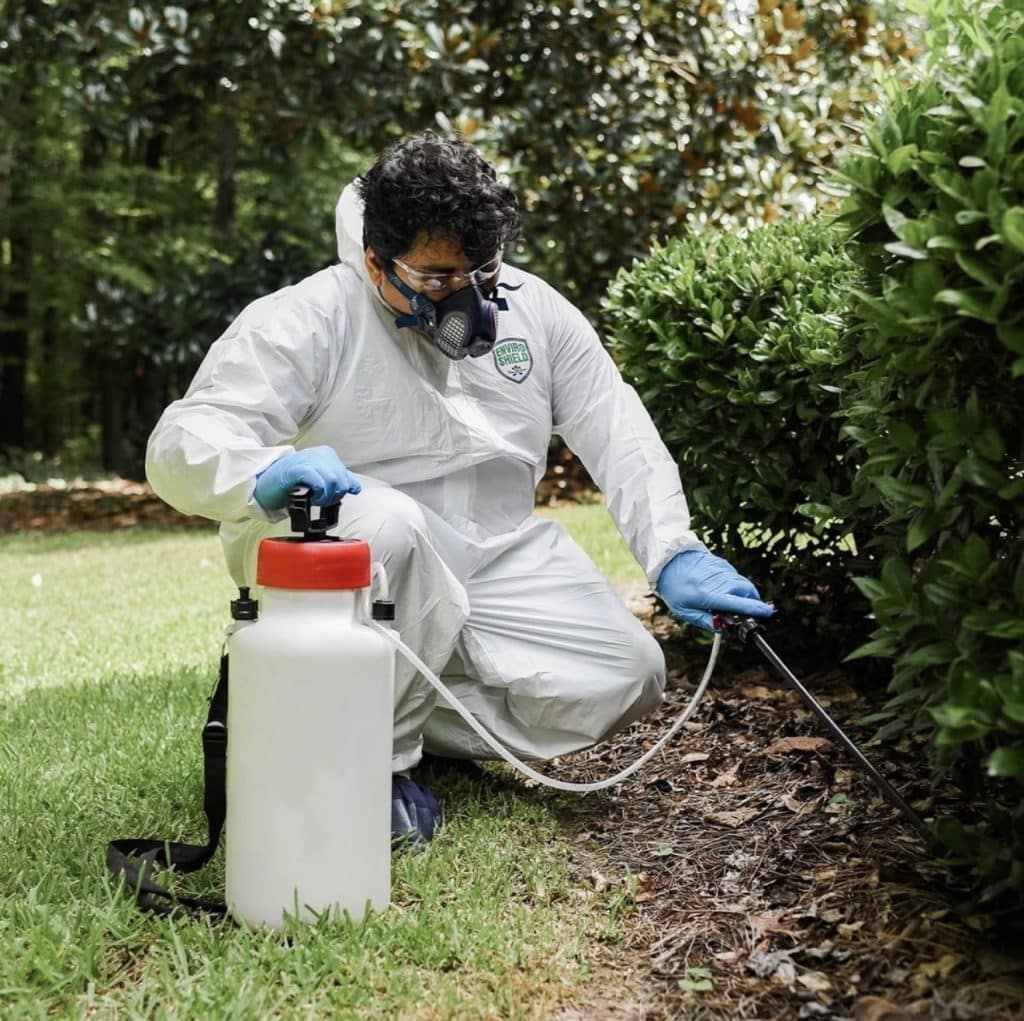 Worker wearing EnviroShield coveralls using sprayer outdoors – ShuBee PPE supplier